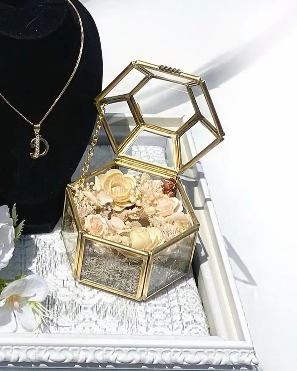 Ring box kaca emas berisi bunga kering peach di atas nampan renda putih