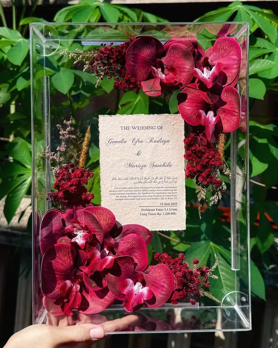 Mahar dalam bingkai akrilik bening dengan anggrek merah marun, difoto di taman