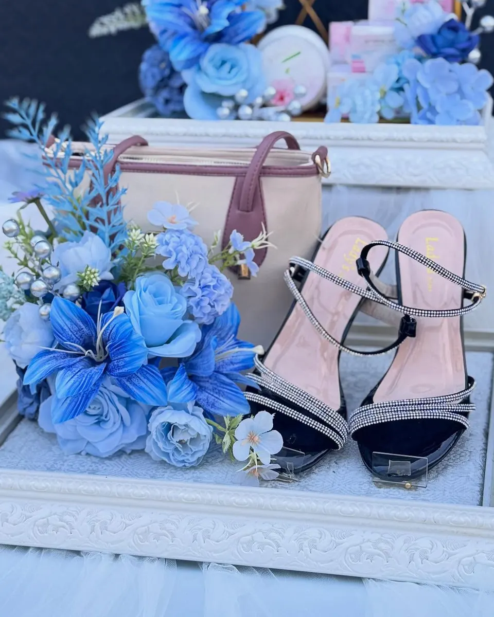 Tas dan sandal hak tinggi di nampan ukir putih, dihias mawar dan lily biru