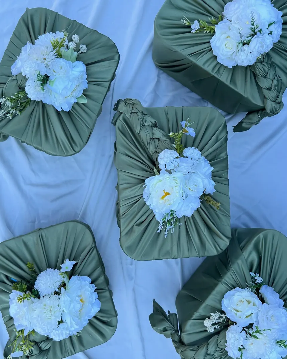 Kotak-kotak dibungkus kain hijau sage dengan hydrangea putih, difoto dari atas
