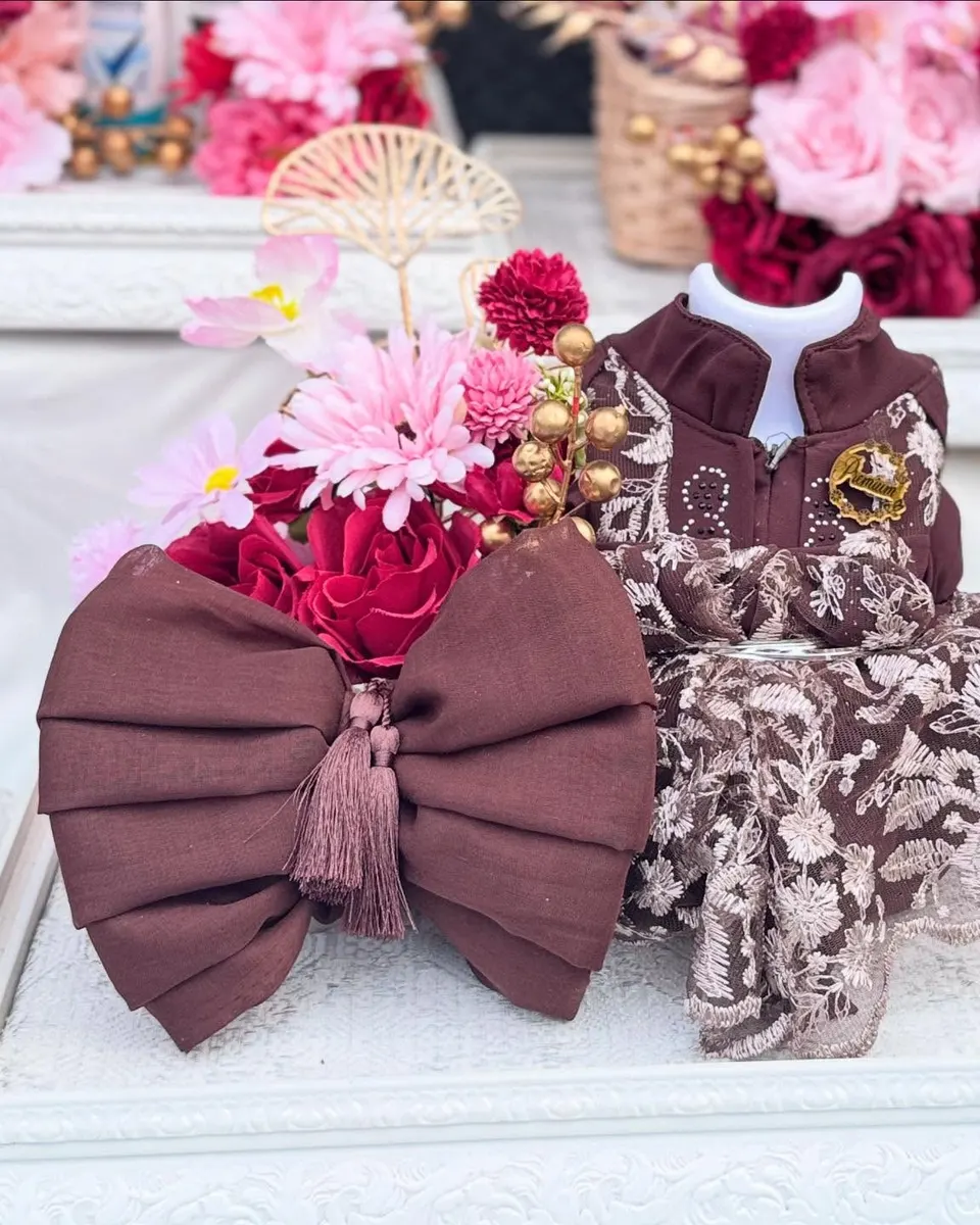 Pita besar cokelat marun dan gamis renda di atas nampan ukir putih, dengan mawar merah