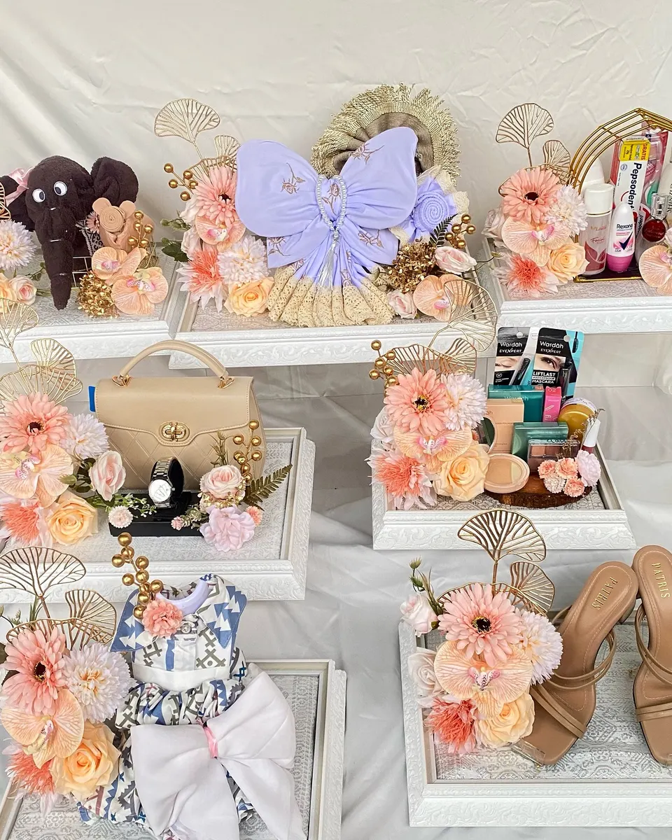 Satu set seserahan di nampan ukir putih: tas, kosmetik, sepatu, dan boneka, dihias gerbera peach dan ginkgo emas